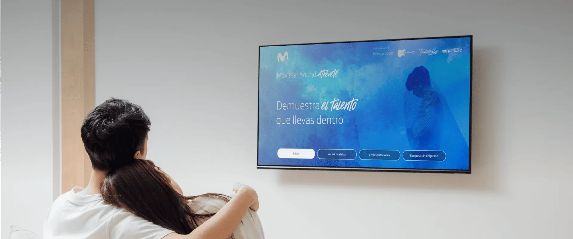 A couple sitting on a sofa watching the LivingApp Movistar platform on a television.